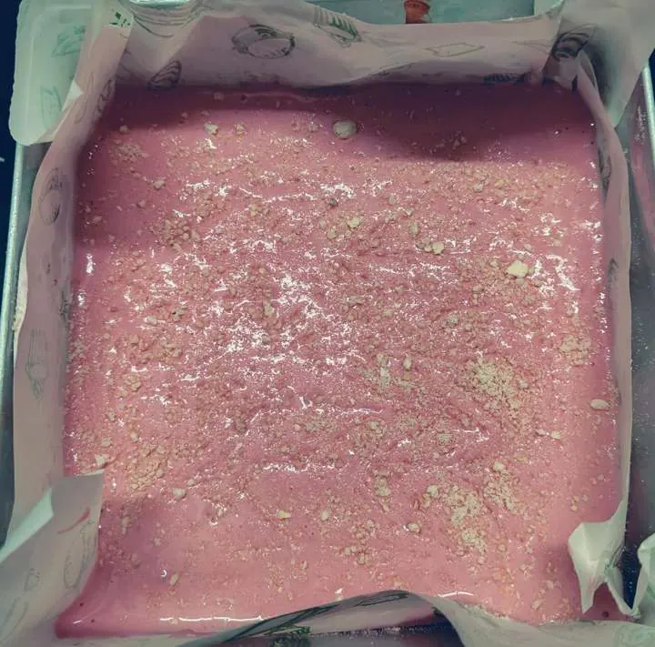 Pink cake batter with crushed nuts in lined tray